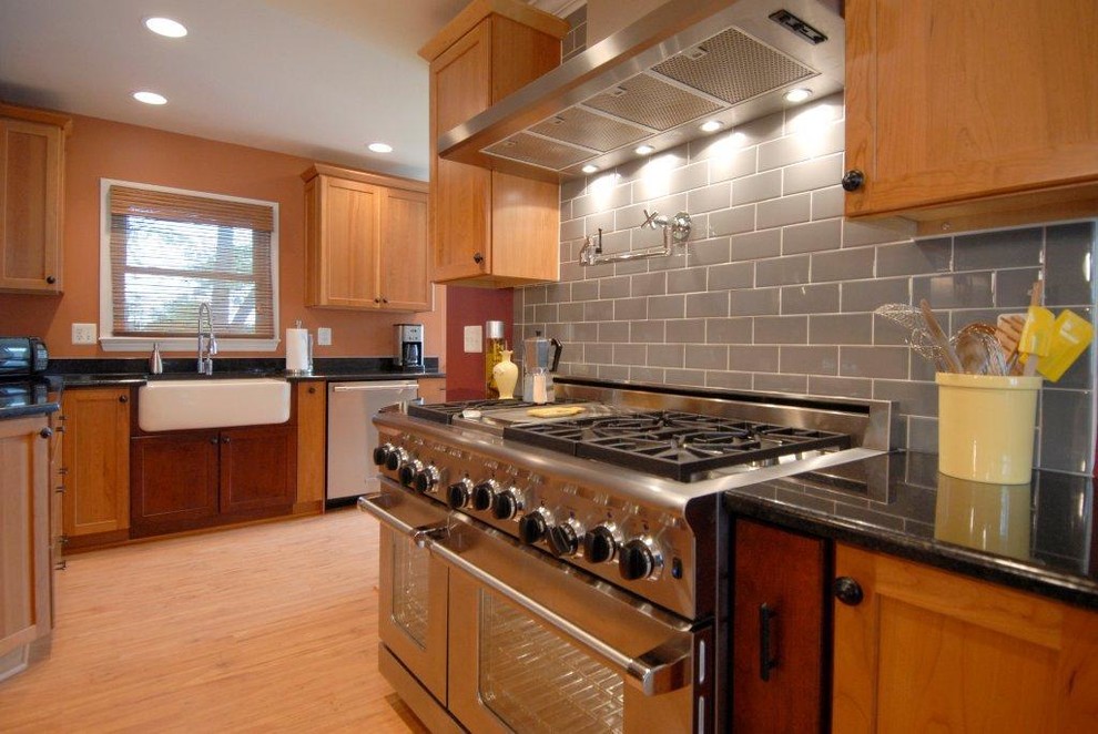Example of a large transitional u-shaped medium tone wood floor eat-in kitchen design in DC Metro with a farmhouse sink, shaker cabinets, medium tone wood cabinets, granite countertops, gray backsplash, subway tile backsplash, stainless steel appliances and a peninsula