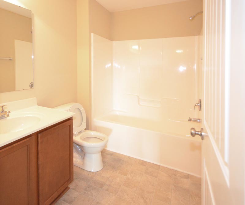 This is an example of a contemporary bathroom in Raleigh with an integrated sink, recessed-panel cabinets, medium wood cabinets, solid surface benchtops, a shower/bathtub combo and a two-piece toilet.