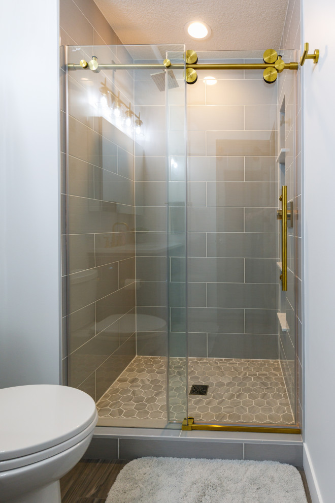 Inspiration for a mid-sized transitional 3/4 bathroom in Minneapolis with recessed-panel cabinets, blue cabinets, an alcove tub, a shower/bathtub combo, a two-piece toilet, gray tile, ceramic tile, white walls, vinyl floors, an undermount sink, engineered quartz benchtops, brown floor, a sliding shower screen, white benchtops, a single vanity and a built-in vanity.