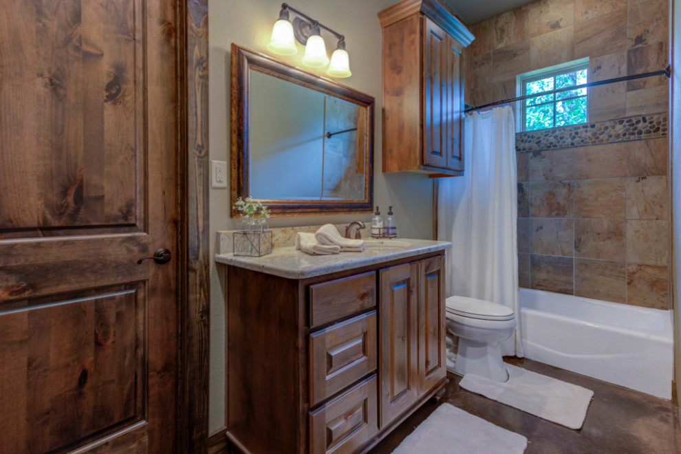 Photo of a mid-sized country kids bathroom in Austin with raised-panel cabinets, dark wood cabinets, a drop-in tub, a curbless shower, a two-piece toilet, multi-coloured tile, porcelain tile, beige walls, concrete floors, an undermount sink, granite benchtops, black floor, a hinged shower door, beige benchtops, a shower seat, a single vanity, a built-in vanity, vaulted and wood walls.