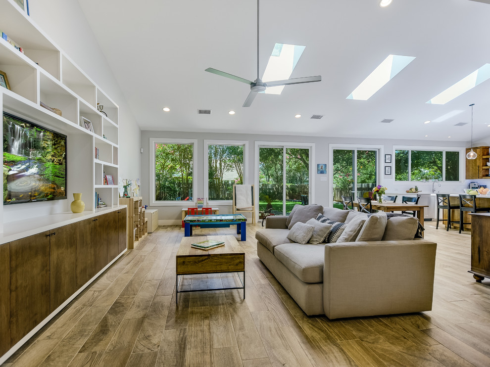 Design ideas for a large contemporary open concept family room in Austin with grey walls, medium hardwood floors, a built-in media wall and brown floor.