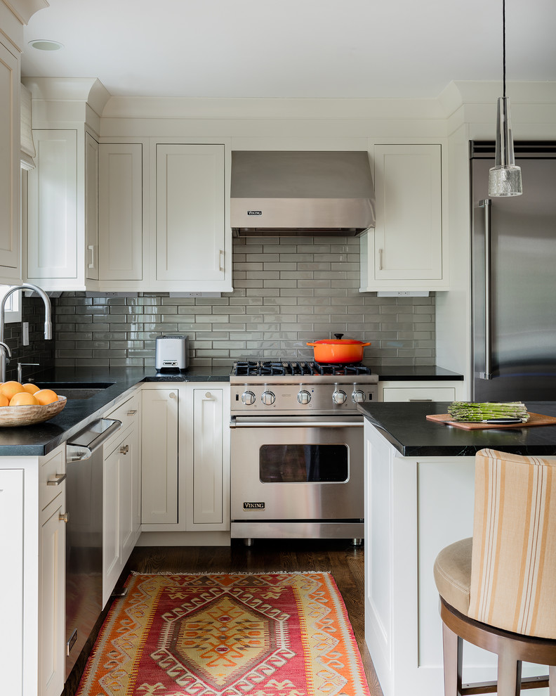 This is an example of a transitional l-shaped kitchen in Boston with an undermount sink, shaker cabinets, white cabinets, grey splashback, subway tile splashback, stainless steel appliances, dark hardwood floors and with island.