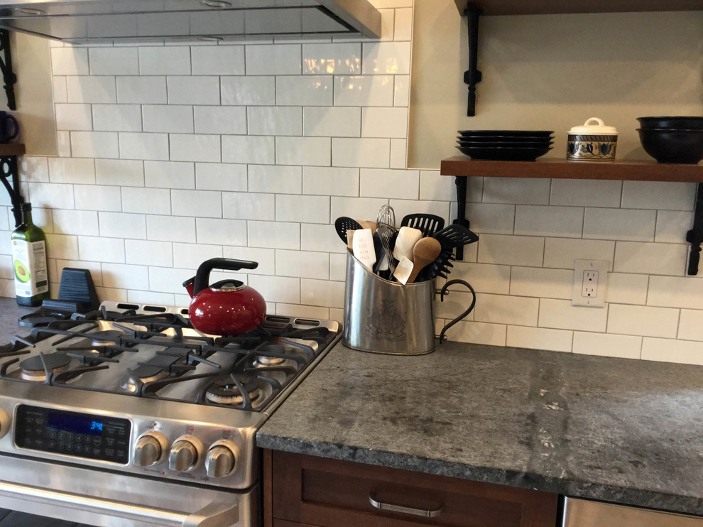 Inspiration for a mid-sized transitional l-shaped kitchen remodel in Ottawa with an undermount sink, shaker cabinets, dark wood cabinets, soapstone countertops, white backsplash, ceramic backsplash, stainless steel appliances and an island