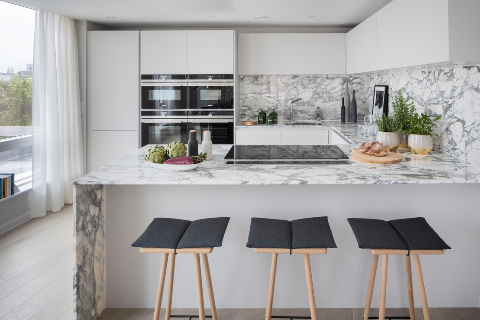 Mid-sized contemporary u-shaped kitchen in London with an undermount sink, flat-panel cabinets, white cabinets, marble benchtops, multi-coloured splashback, marble splashback, stainless steel appliances, light hardwood floors, a peninsula, beige floor and multi-coloured benchtop.