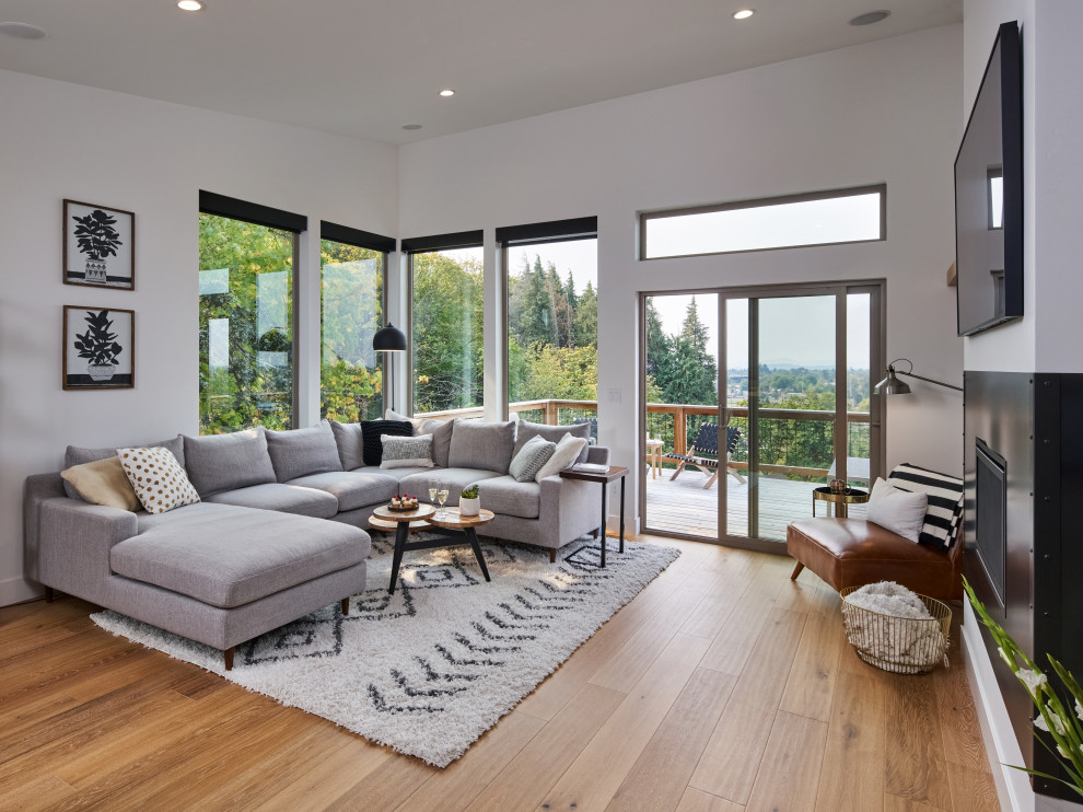 This is an example of a mid-sized modern open concept living room in Other with white walls, light hardwood floors, a hanging fireplace, a metal fireplace surround, a wall-mounted tv, brown floor and vaulted.