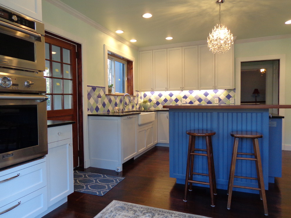 Mid-sized transitional l-shaped enclosed kitchen photo in Raleigh with shaker cabinets, white cabinets, soapstone countertops, blue backsplash, ceramic backsplash, white appliances and an island