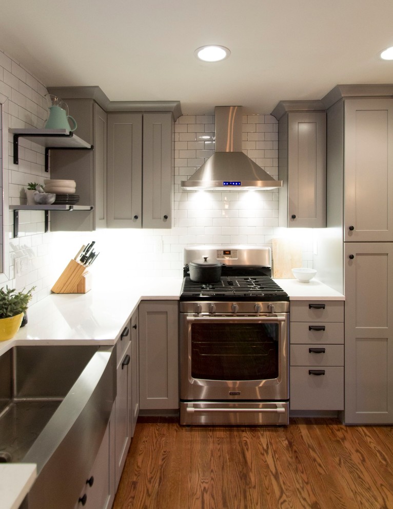 Example of a mid-sized transitional l-shaped medium tone wood floor eat-in kitchen design in Denver with a farmhouse sink, shaker cabinets, gray cabinets, quartz countertops, white backsplash, ceramic backsplash, stainless steel appliances and an island