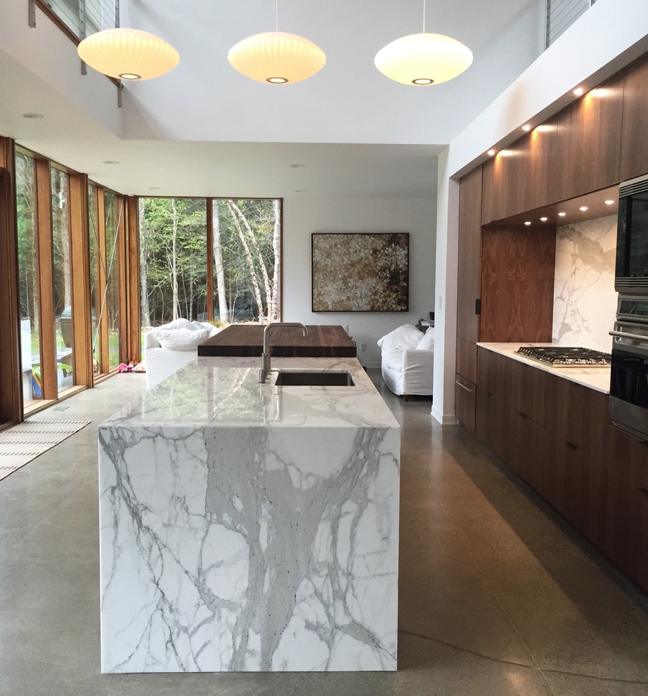 This is an example of a large modern open plan kitchen in New York with an undermount sink, flat-panel cabinets, brown cabinets, marble benchtops, white splashback, stone slab splashback, stainless steel appliances, concrete floors and with island.