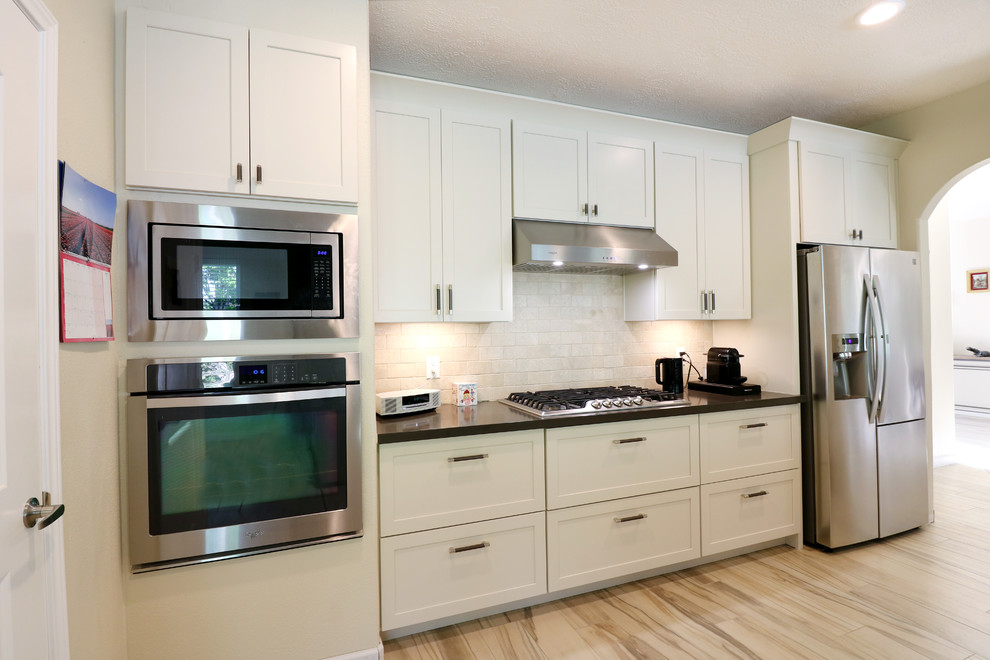 Inspiration for a mid-sized transitional u-shaped porcelain tile and beige floor eat-in kitchen remodel in Houston with an undermount sink, recessed-panel cabinets, white cabinets, soapstone countertops, white backsplash, subway tile backsplash, stainless steel appliances, an island and black countertops