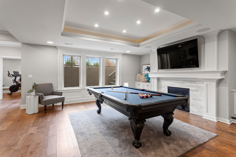 Design ideas for a large classic walk-out basement in Kansas City with grey walls, medium hardwood flooring, brown floors, a game room, a standard fireplace, a tiled fireplace surround and a drop ceiling.