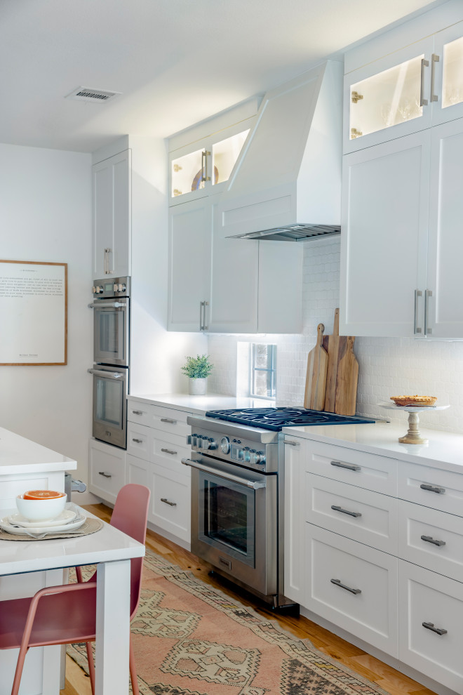Eat-in kitchen - large transitional l-shaped light wood floor and brown floor eat-in kitchen idea in Austin with a single-bowl sink, shaker cabinets, white cabinets, quartz countertops, white backsplash, ceramic backsplash, stainless steel appliances, an island and white countertops
