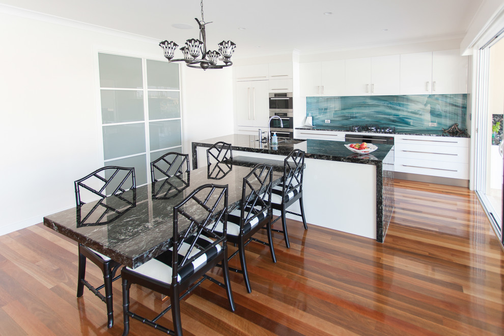Contemporary single-wall eat-in kitchen in Gold Coast - Tweed with medium hardwood floors, an undermount sink, flat-panel cabinets, white cabinets, marble benchtops, blue splashback, glass sheet splashback, stainless steel appliances and with island.