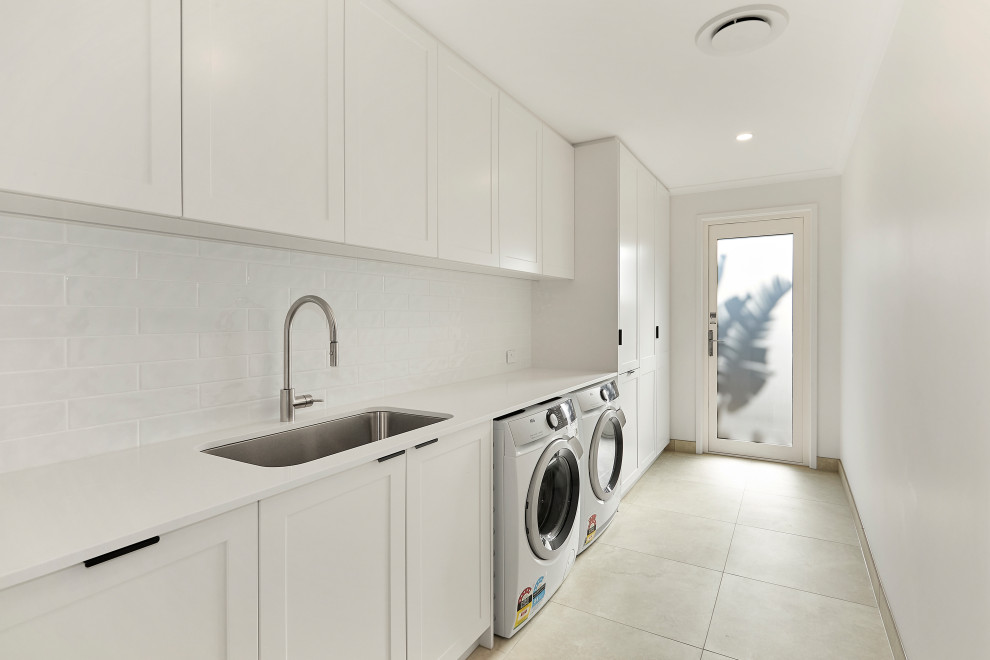 Immagine di un'ampia sala lavanderia minimal con lavello da incasso, ante in legno chiaro, pareti bianche e top bianco