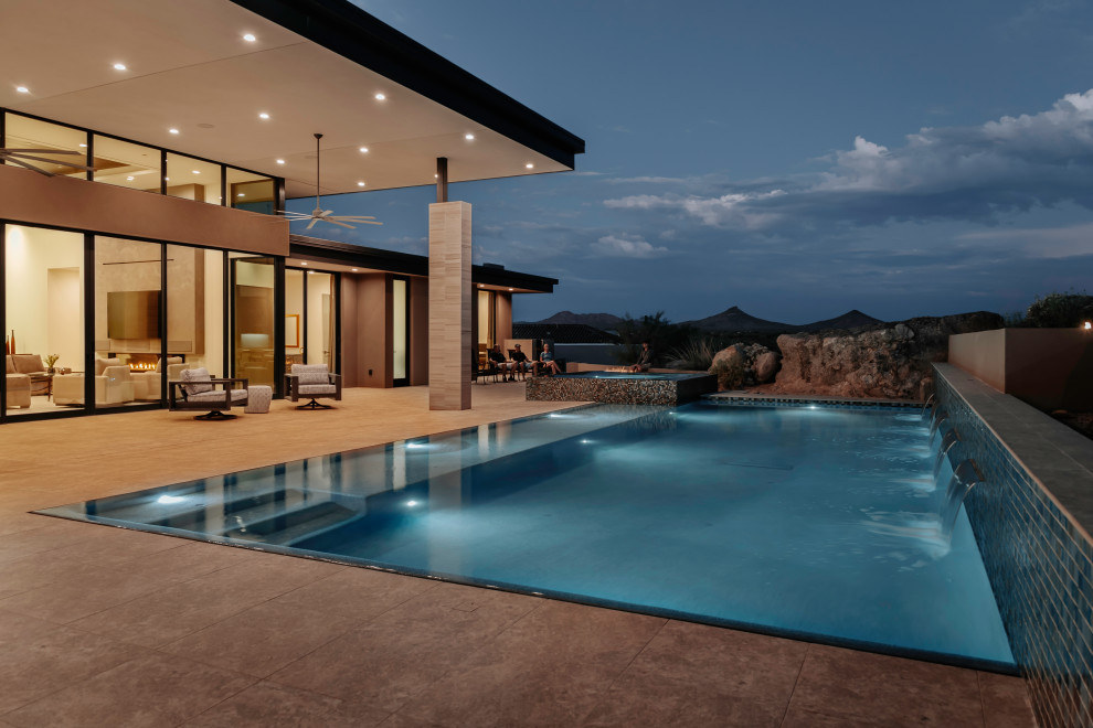 Imagen de piscina infinita contemporánea grande rectangular en patio trasero con paisajismo de piscina y suelo de baldosas