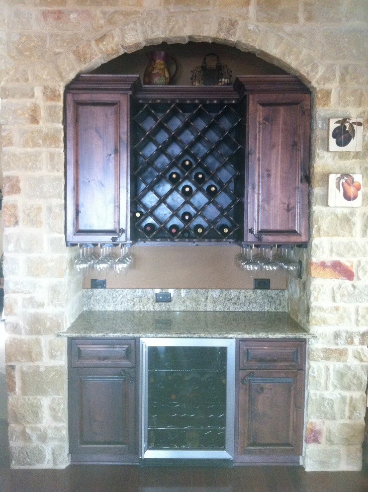 This is an example of a small traditional single-wall wet bar in Austin with raised-panel cabinets, dark wood cabinets, granite benchtops, multi-coloured splashback, dark hardwood floors, brown floor and beige benchtop.
