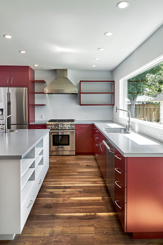 Inspiration for a mid-sized contemporary u-shaped open plan kitchen in San Francisco with an undermount sink, flat-panel cabinets, red cabinets, solid surface benchtops, grey splashback, stainless steel appliances, medium hardwood floors, with island, brown floor and grey benchtop.