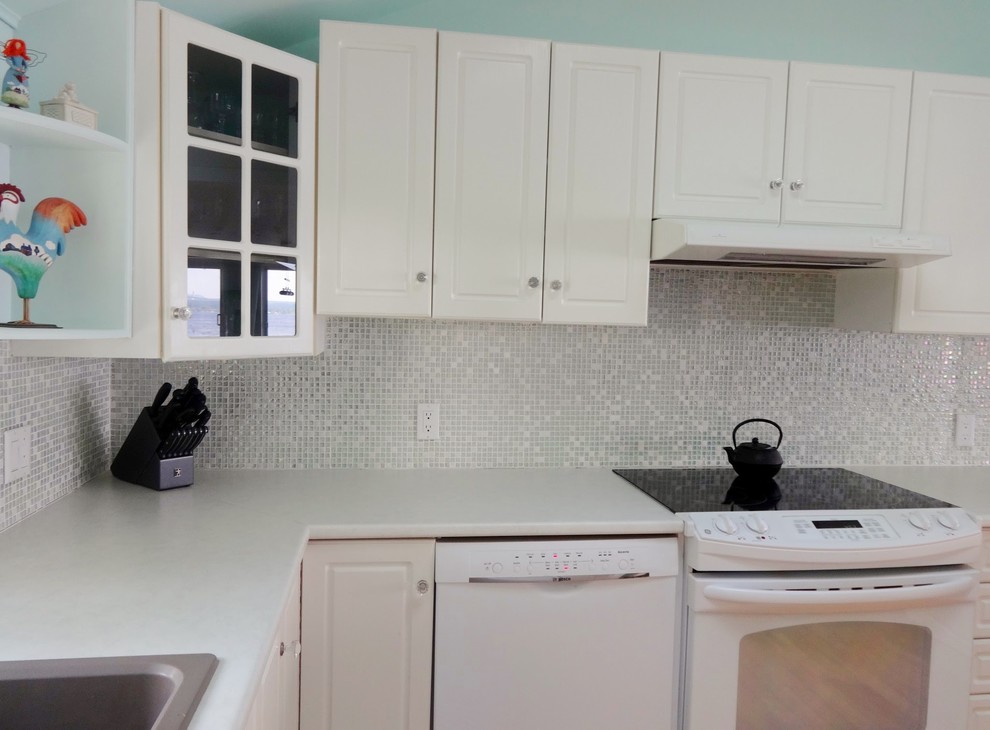 Photo of a small beach style u-shaped open plan kitchen in Montreal with a double-bowl sink, shaker cabinets, laminate benchtops, white splashback, mosaic tile splashback, light hardwood floors and no island.