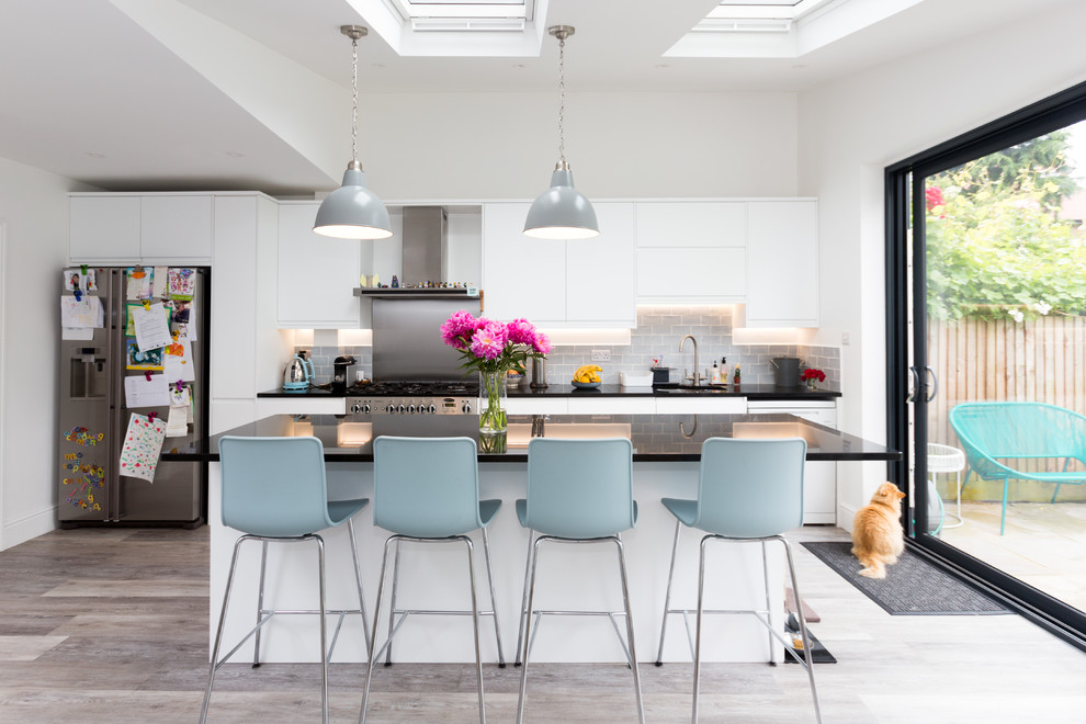 Inspiration for a contemporary galley eat-in kitchen in London with an undermount sink, flat-panel cabinets, white cabinets, grey splashback, subway tile splashback, stainless steel appliances, medium hardwood floors, with island, grey floor and black benchtop.