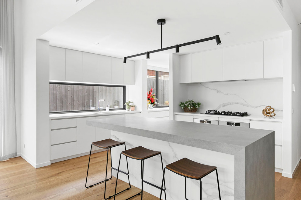 Design ideas for a contemporary l-shaped kitchen in Melbourne with an undermount sink, flat-panel cabinets, white cabinets, medium hardwood floors, with island, brown floor and grey benchtop.