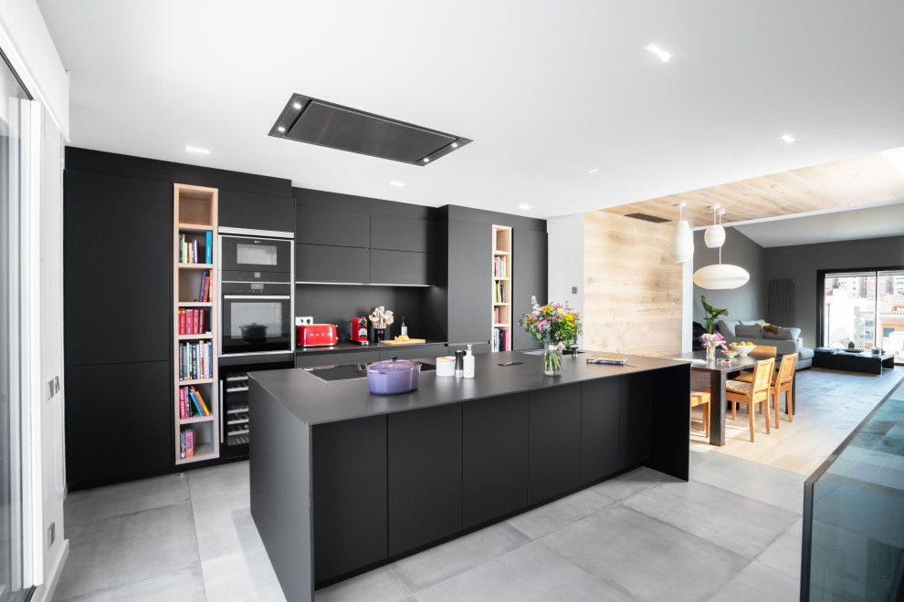 This is an example of a large contemporary galley open plan kitchen in Other with flat-panel cabinets, black cabinets, black splashback, with island, grey floor, black benchtop, an undermount sink and black appliances.