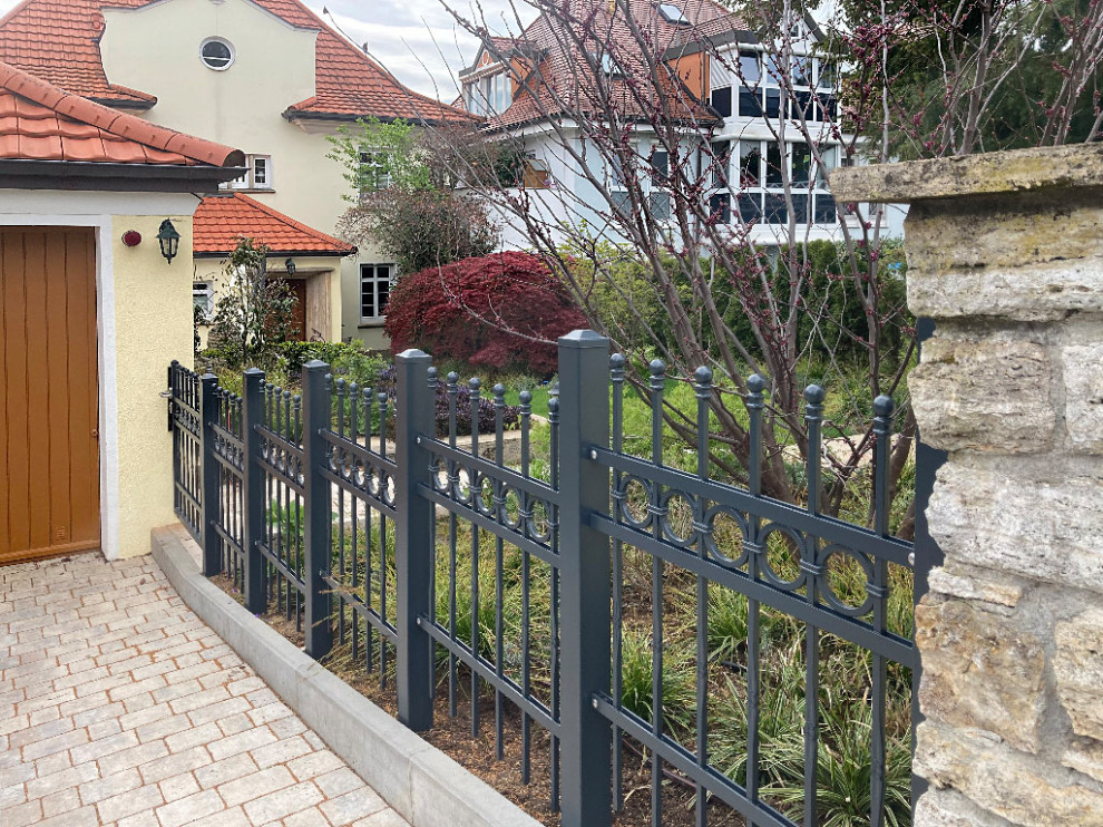 Ispirazione per un giardino tradizionale esposto in pieno sole davanti casa in estate con un muro di contenimento, pavimentazioni in pietra naturale e recinzione in metallo