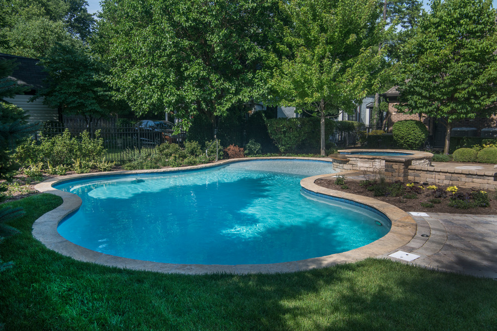 This is an example of a mid-sized country backyard custom-shaped natural pool in Chicago with a hot tub and natural stone pavers.