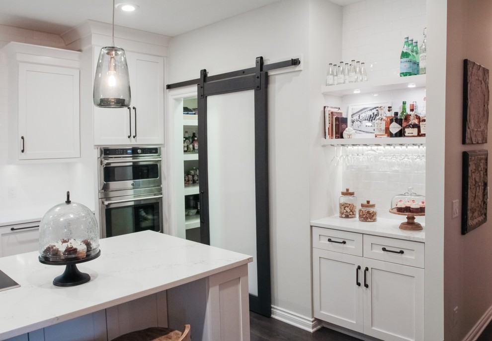 Mid-sized transitional galley eat-in kitchen in Grand Rapids with a farmhouse sink, shaker cabinets, white cabinets, quartz benchtops, white splashback, ceramic splashback, stainless steel appliances, dark hardwood floors and with island.
