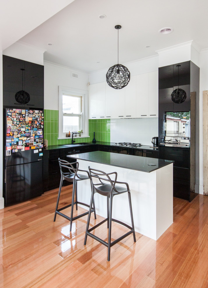Inspiration for a contemporary l-shaped kitchen in Melbourne with a drop-in sink, flat-panel cabinets, black cabinets, green splashback, medium hardwood floors, with island, brown floor and black benchtop.
