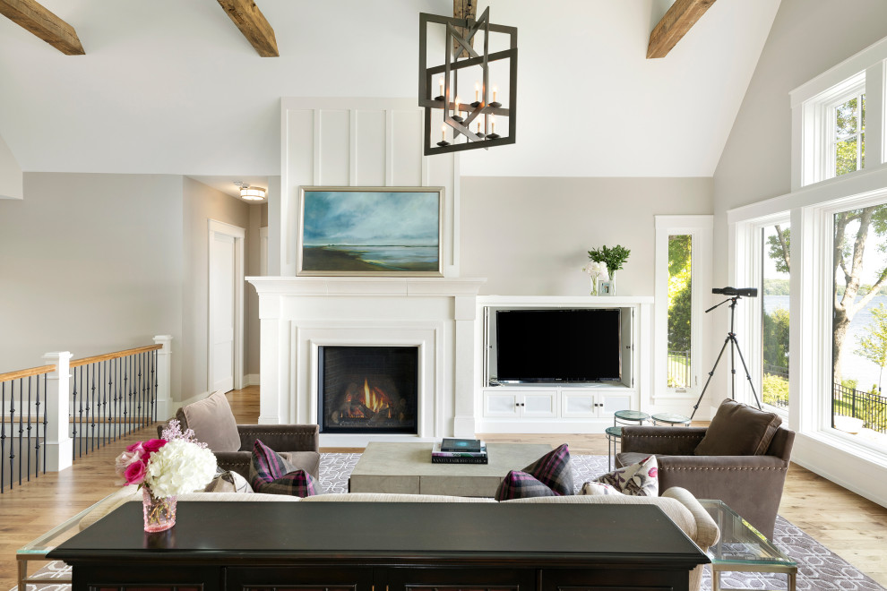 Mid-sized beach style formal living room in Minneapolis with beige walls, medium hardwood floors, a standard fireplace, a wood fireplace surround, a built-in media wall, brown floor and vaulted.