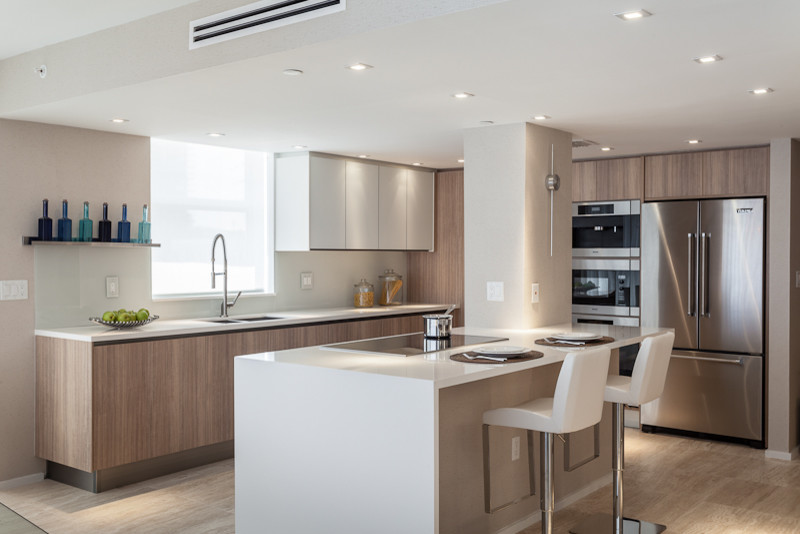 This is an example of a mid-sized contemporary l-shaped eat-in kitchen in Miami with a double-bowl sink, flat-panel cabinets, white cabinets, solid surface benchtops, white splashback, subway tile splashback, light hardwood floors and with island.