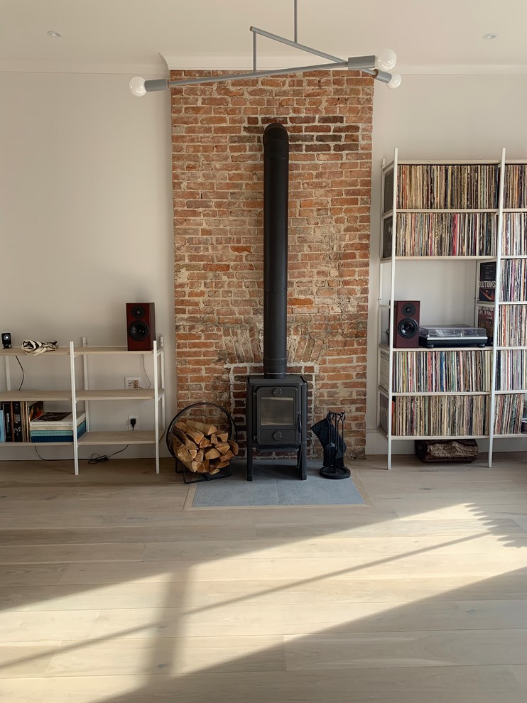 This is an example of a mid-sized industrial open concept family room in New York with white walls, light hardwood floors, a wood stove, a tile fireplace surround, white floor and no tv.