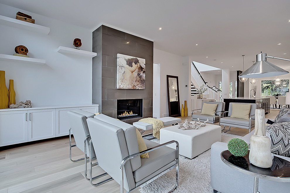 Photo of a scandinavian open concept family room in Calgary with white walls, light hardwood floors, a standard fireplace and a tile fireplace surround.