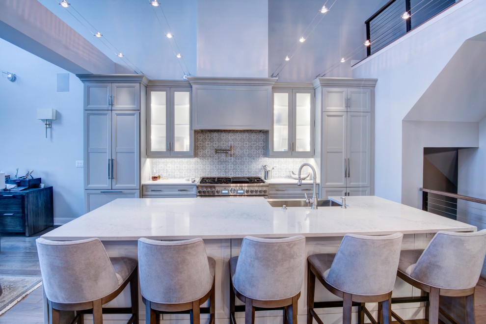 Large contemporary single-wall open plan kitchen in New York with a farmhouse sink, recessed-panel cabinets, white cabinets, quartzite benchtops, multi-coloured splashback, cement tile splashback, panelled appliances, light hardwood floors, with island, beige floor and white benchtop.