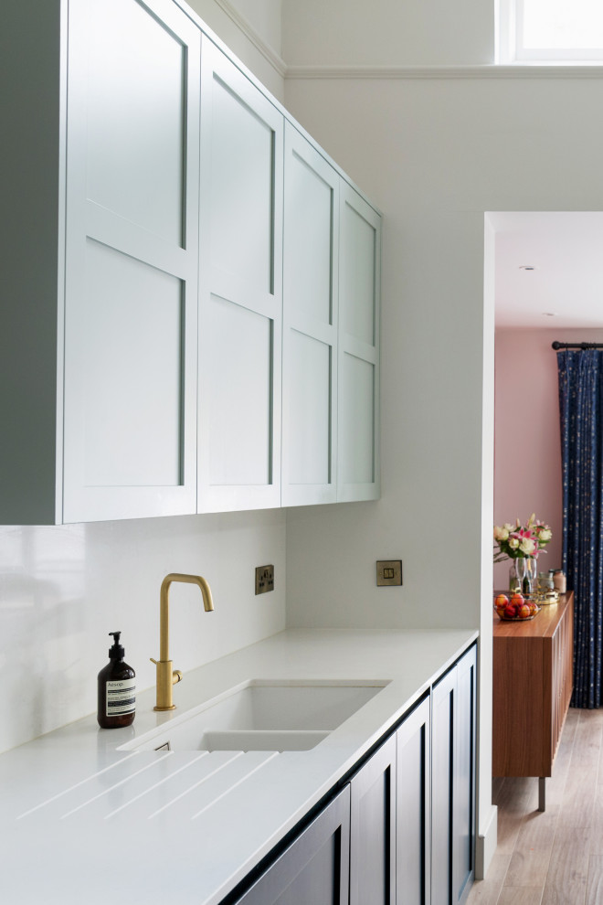 Inspiration for a mid-sized transitional kitchen in London with shaker cabinets, blue cabinets, solid surface benchtops, white splashback, with island and white benchtop.