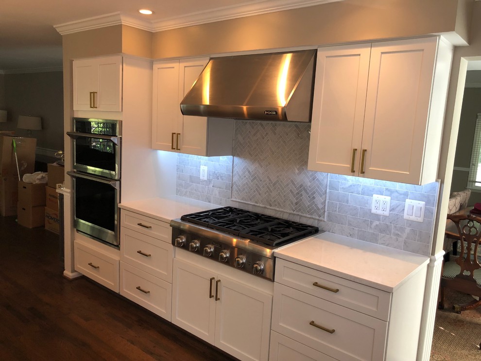 Example of a mid-sized transitional u-shaped dark wood floor and brown floor eat-in kitchen design in DC Metro with a farmhouse sink, recessed-panel cabinets, white cabinets, quartz countertops, white backsplash, marble backsplash, stainless steel appliances, an island and white countertops