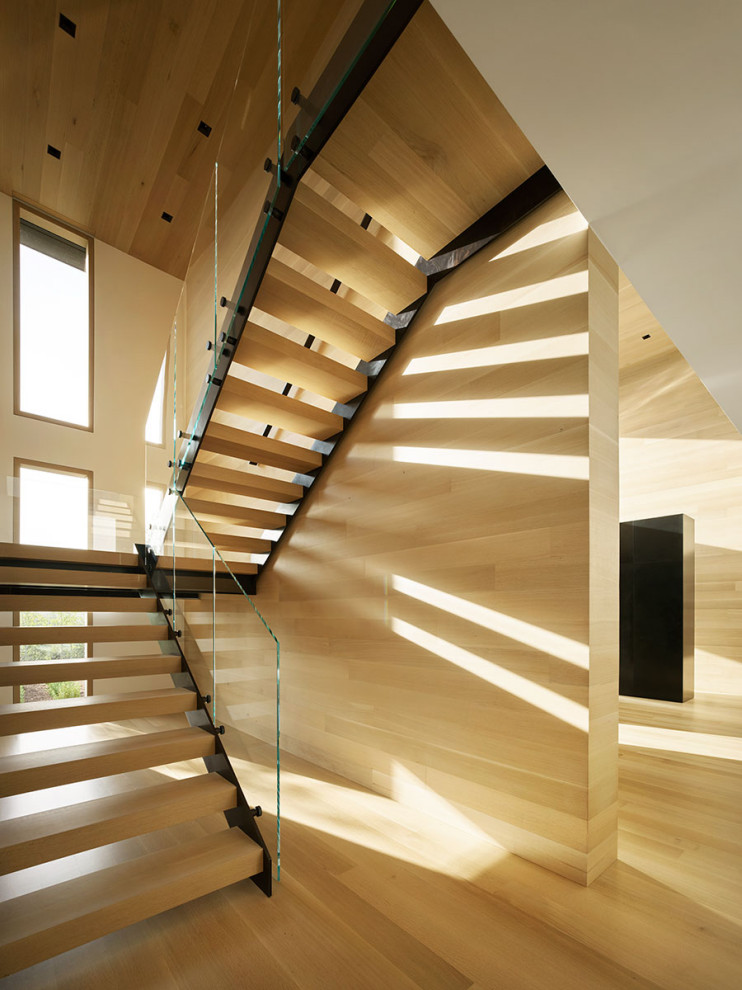 Ejemplo de escalera moderna con escalones de madera, barandilla de vidrio y madera