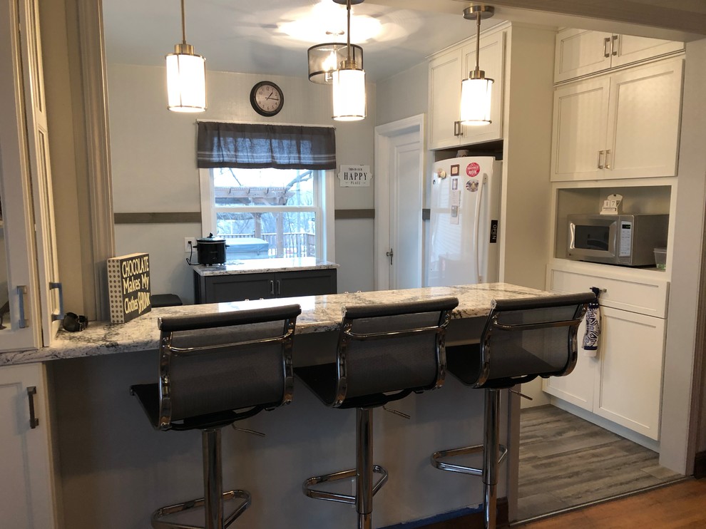Example of a small transitional l-shaped laminate floor and gray floor eat-in kitchen design with an undermount sink, flat-panel cabinets, white cabinets, quartz countertops, gray backsplash, subway tile backsplash, white appliances and white countertops