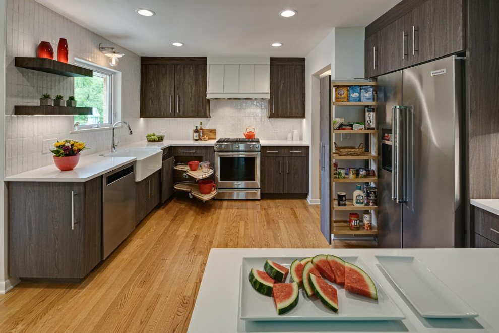 Example of a small mid-century modern l-shaped light wood floor and brown floor kitchen pantry design in Chicago with a farmhouse sink, flat-panel cabinets, dark wood cabinets, quartz countertops, white backsplash, ceramic backsplash, stainless steel appliances and white countertops