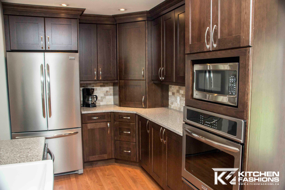 Large transitional u-shaped medium tone wood floor open concept kitchen photo with a farmhouse sink, shaker cabinets, dark wood cabinets, quartz countertops, brown backsplash, stone tile backsplash, stainless steel appliances and an island