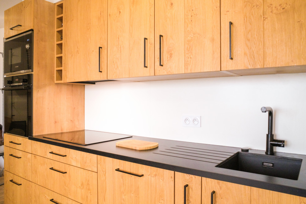 Foto de cocina lineal moderna de tamaño medio abierta sin isla con puertas de armario de madera clara, electrodomésticos negros, encimeras negras y fregadero integrado
