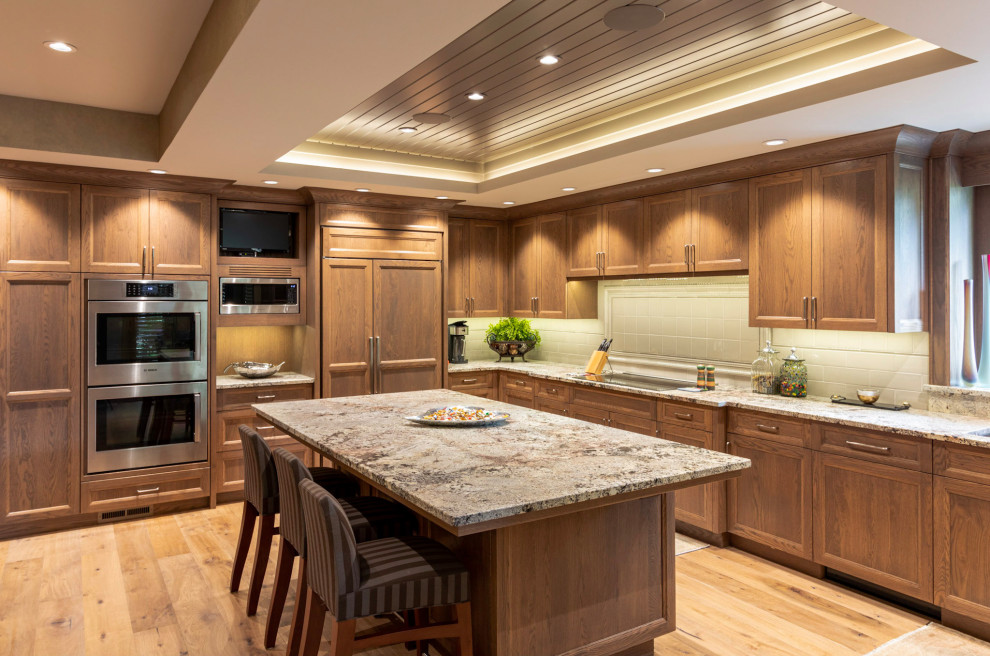 This is an example of a transitional u-shaped kitchen in Omaha with an undermount sink, recessed-panel cabinets, medium wood cabinets, grey splashback, panelled appliances, medium hardwood floors, with island, brown floor, grey benchtop and recessed.