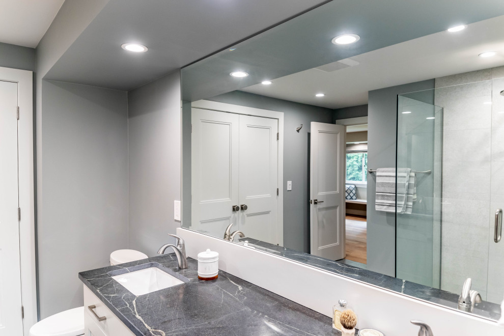 Large transitional master bathroom in Seattle with recessed-panel cabinets, white cabinets, a corner shower, a one-piece toilet, gray tile, ceramic tile, grey walls, ceramic floors, an undermount sink, quartzite benchtops, grey floor, a hinged shower door, grey benchtops, a double vanity and a freestanding vanity.