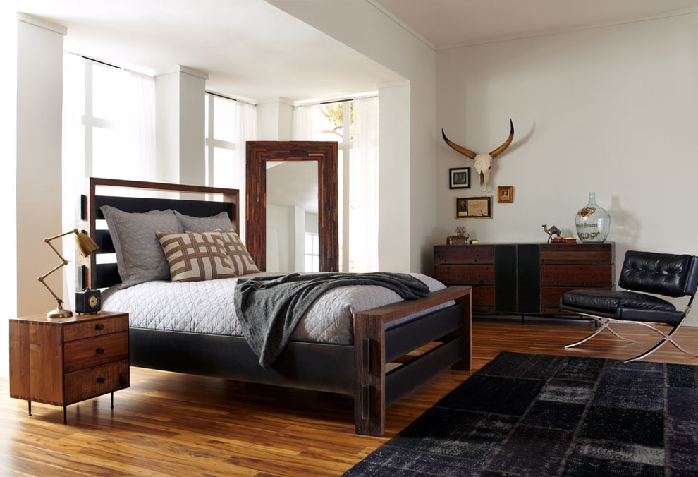 Mid-sized industrial master bedroom in New York with white walls and medium hardwood floors.
