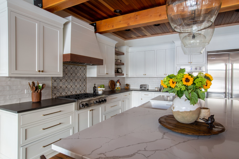 This is an example of a large rustic l-shaped kitchen/diner in New York with shaker cabinets, white cabinets, engineered stone countertops, white splashback, metro tiled splashback, stainless steel appliances, an island and exposed beams.