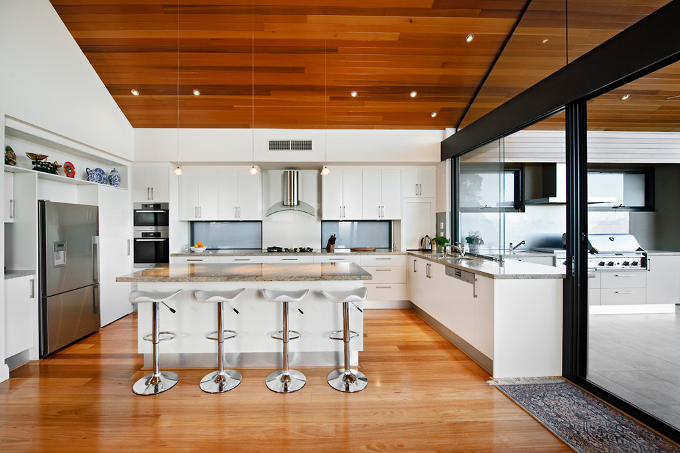 Large modern u-shaped eat-in kitchen in Perth with stainless steel appliances, a drop-in sink, flat-panel cabinets, white cabinets, quartz benchtops, medium hardwood floors and with island.