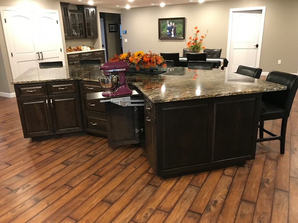 Example of a large classic galley dark wood floor and brown floor open concept kitchen design with an undermount sink, raised-panel cabinets, dark wood cabinets, granite countertops, stainless steel appliances and an island