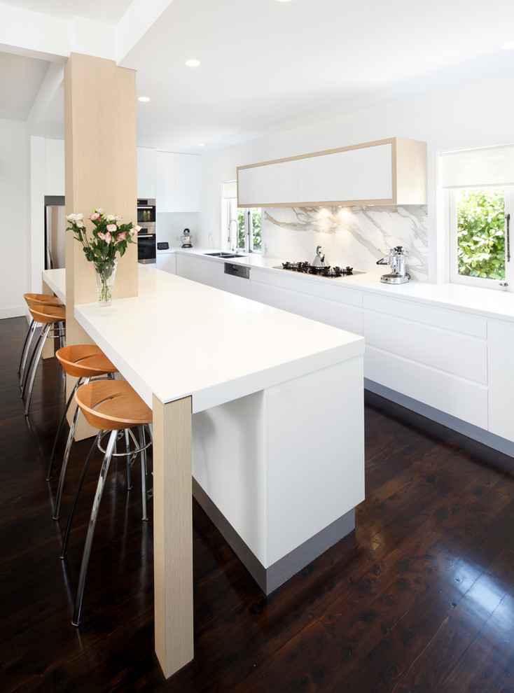 This is an example of a modern l-shaped kitchen in Sydney with a drop-in sink, flat-panel cabinets, white cabinets, solid surface benchtops, stone slab splashback and stainless steel appliances.