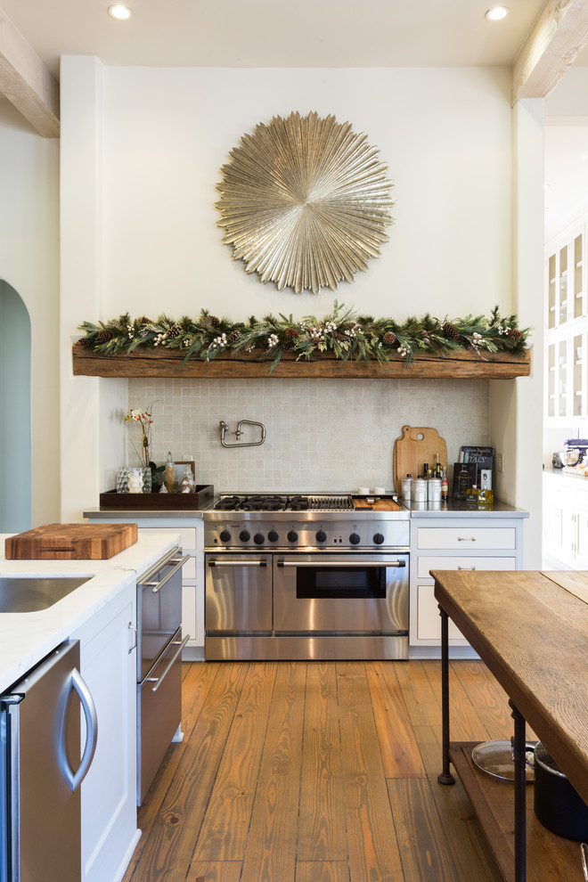 Example of a mountain style medium tone wood floor and brown floor open concept kitchen design in Houston with white cabinets, marble countertops, beige backsplash, stainless steel appliances, two islands and white countertops