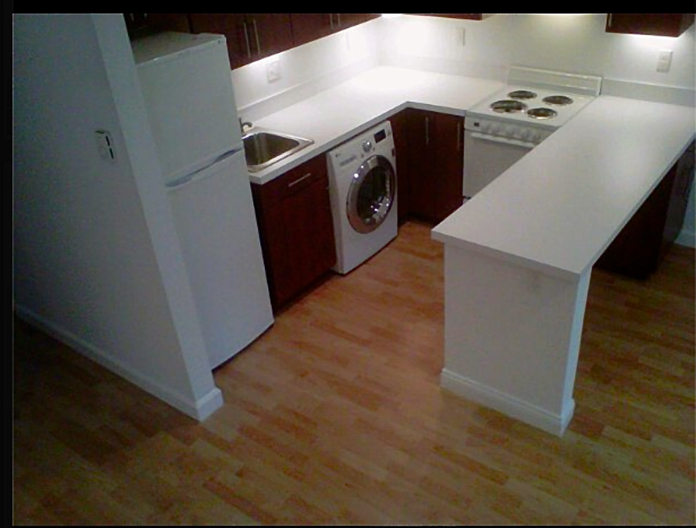 This is an example of a small traditional u-shaped separate kitchen in Providence with flat-panel cabinets, dark wood cabinets, laminate benchtops, white appliances, a drop-in sink, a peninsula, white splashback and light hardwood floors.