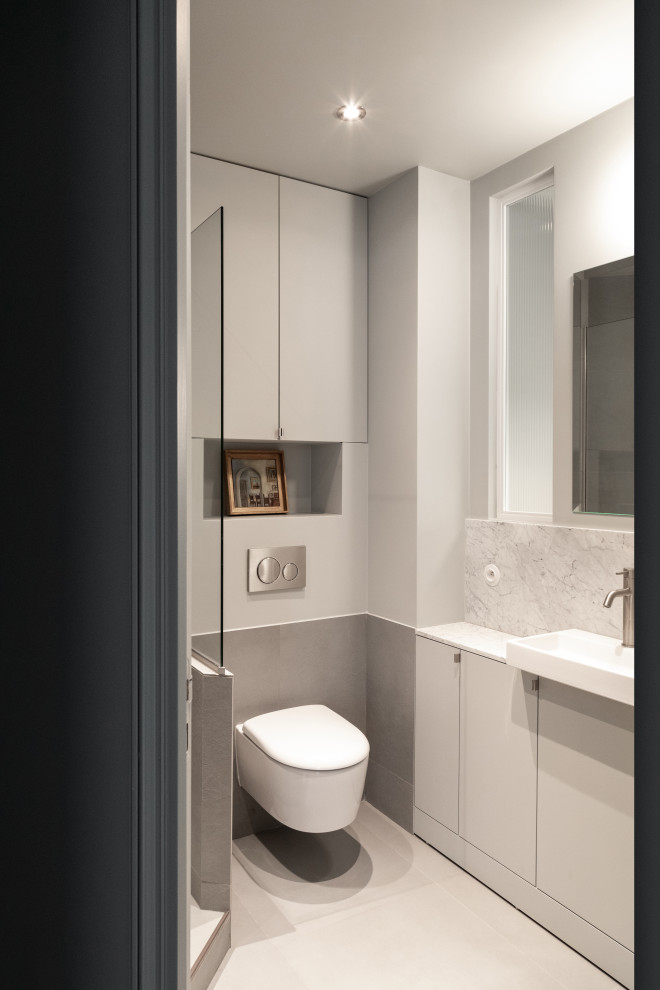 Photo of a mid-sized contemporary bathroom in Paris with beaded inset cabinets, grey cabinets, an alcove shower, a wall-mount toilet, white tile, ceramic tile, grey walls, ceramic floors, an undermount sink, tile benchtops, beige floor, white benchtops, a niche, a single vanity and wood.